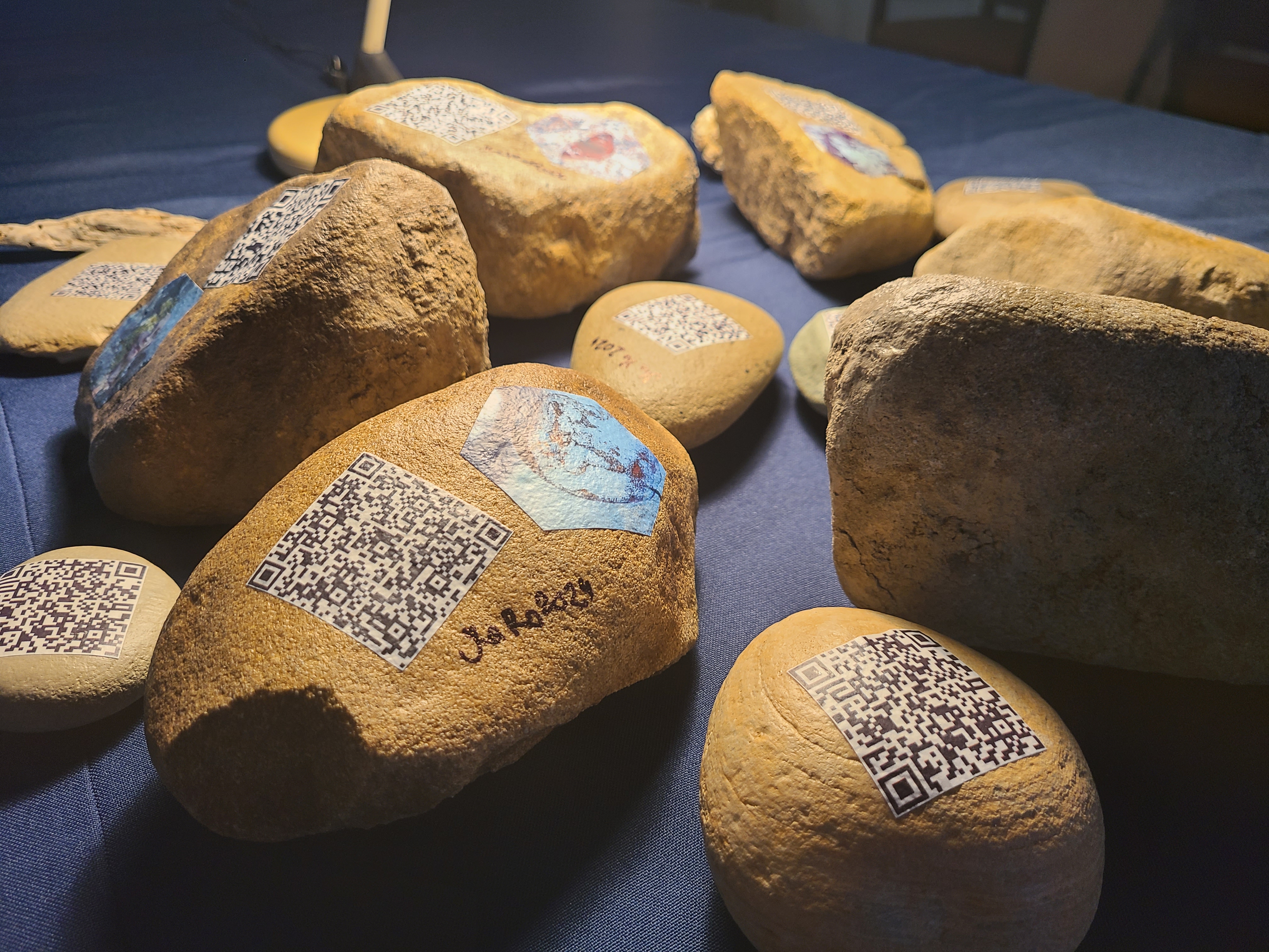 A group of stones on a blue tablecloth with QR codes pasted to them. 